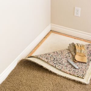 Construction Gloves and Utility Knife On Pulled Back Carpet and Pad In Room.