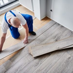 Man installing laminate wood flooring in apartment under renovation.
