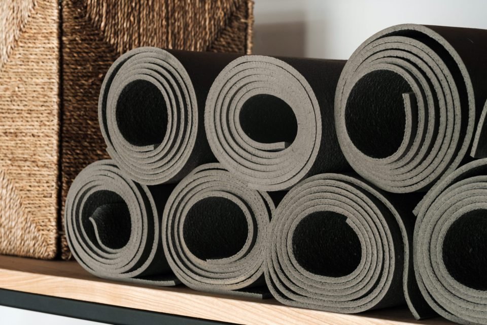 Gray yoga mats lying on a shelf, rolled up