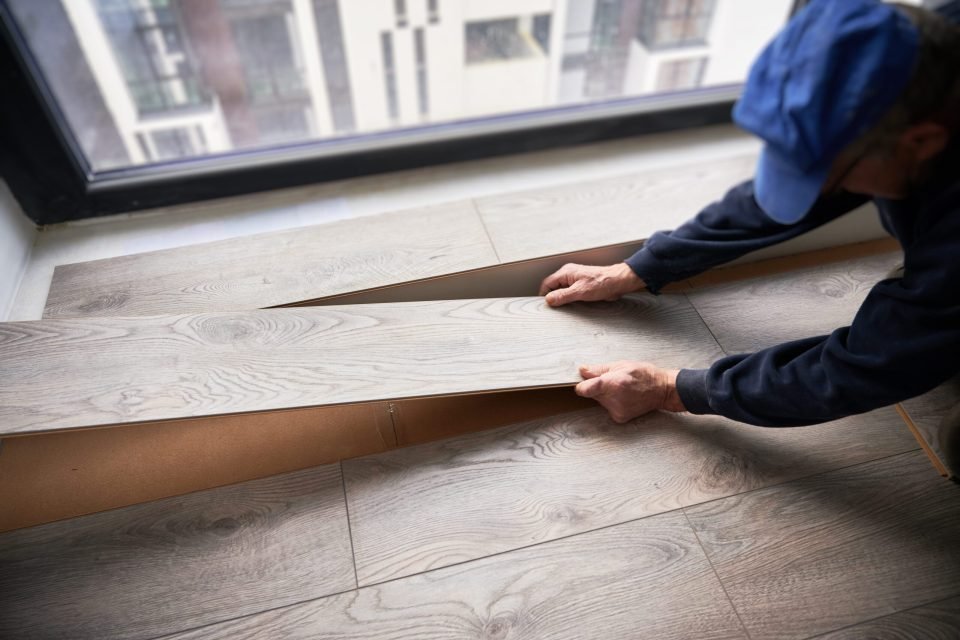 Man laying laminate flooring in apartment under renovation.
